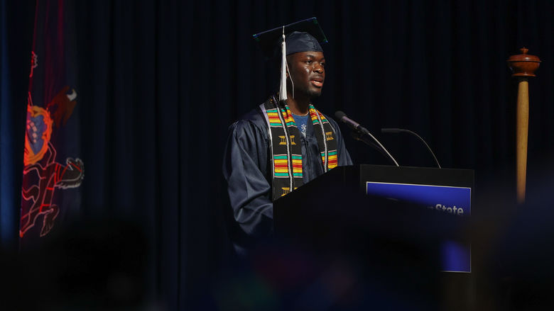 A person wearing a graduation gown speaks at commencement.