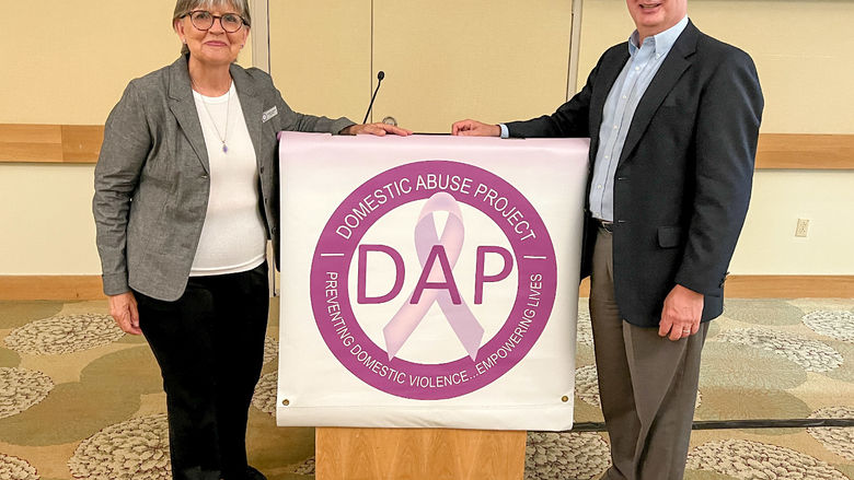A woman and a man stand next to a lectern with a Domestic Abuse Project banner in the center.