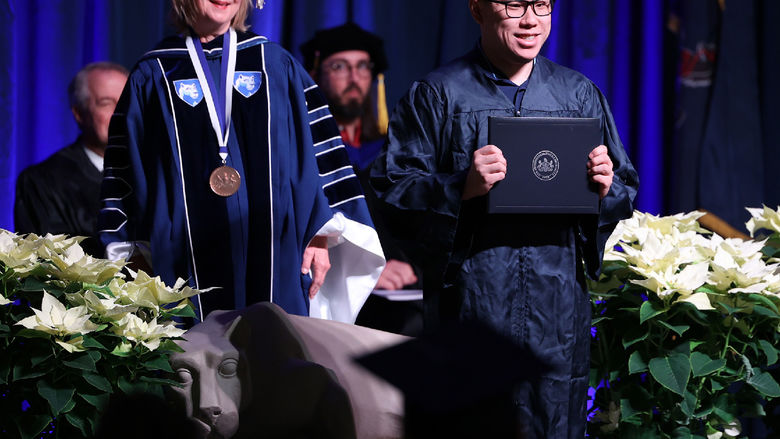 A man stands on a stage holding a diploma cover.