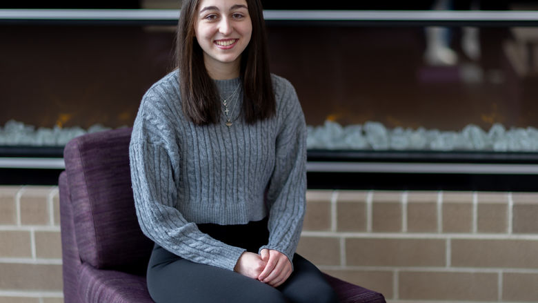 A female student sits on a chair in front of a fireplace.
