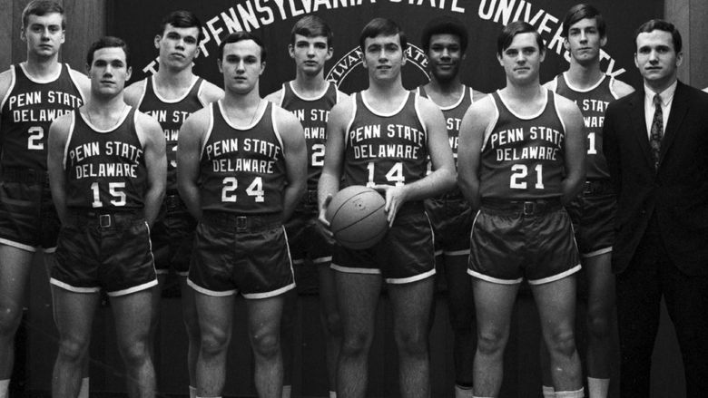 A group of men's basketball players stands in front of a Penn State banner.