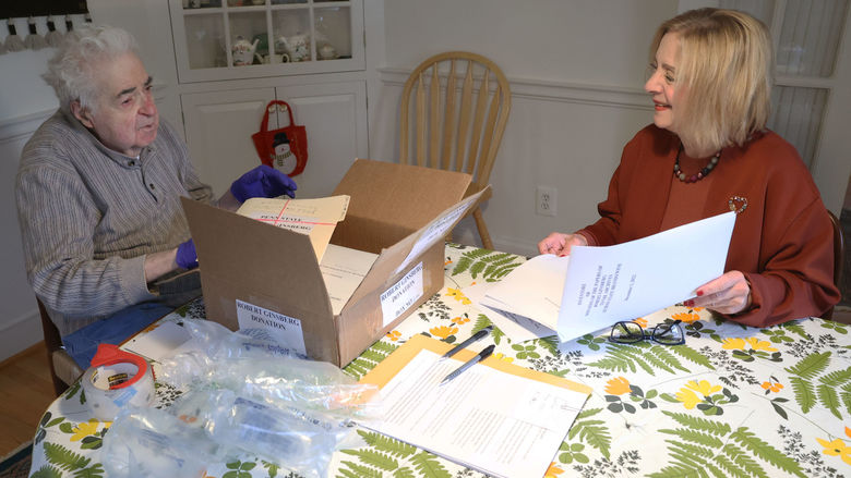 A man and a woman sit at a dining room table look at files.
