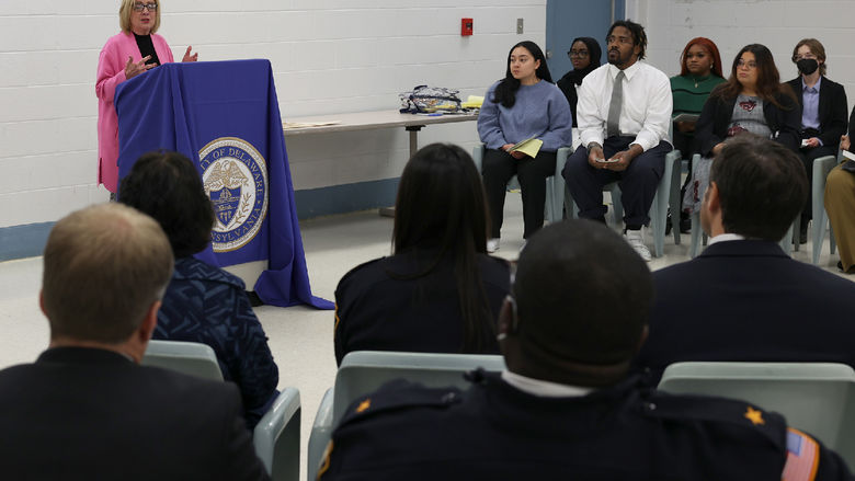 A woman at a lectern speaks to a group of people seated.