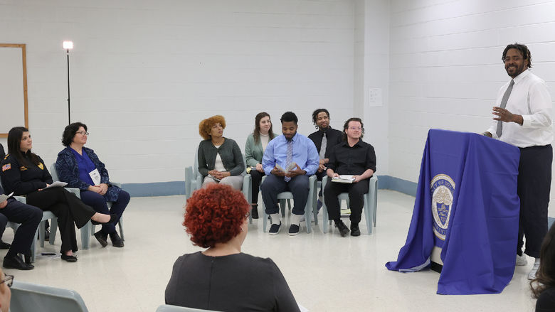 A man stands at a lectern speaking to a group of people seating.