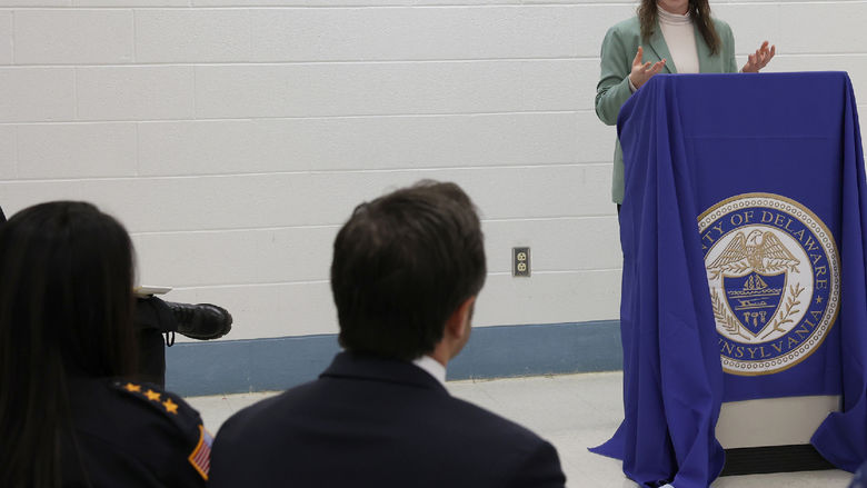 A woman stands at a lectern and speaks to a group of people seated.