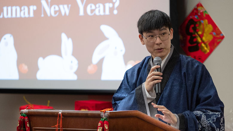 A male student stands at a podium wearing a traditional Chinese robe.