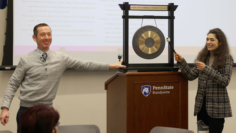 A female student bangs a gong while a male holds it.