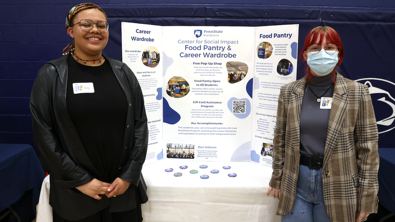 two students standing in front of a poster for the center for social impact