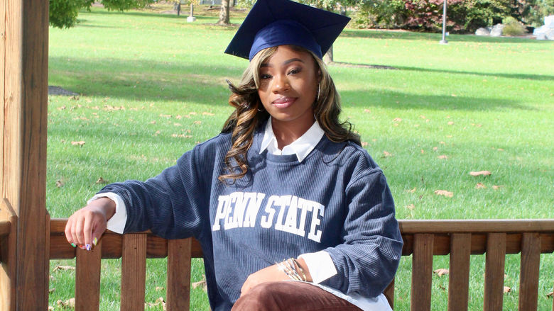 A students wearing a graduation cap sitting on an outside bench.