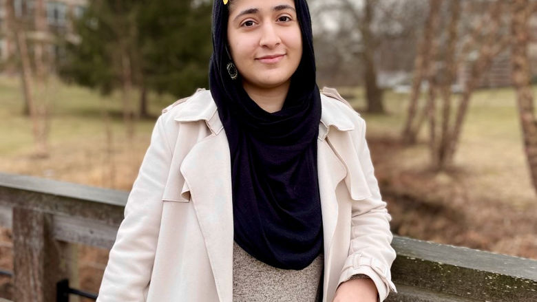 Rabia Rafiqzadah stands on a bridge wearing a black scarf and white coat. 