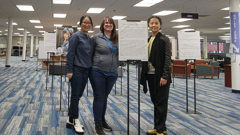 Three women standing in front of sign for exhibit