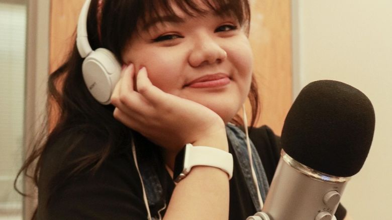 Victoria Pham sits with her chin resting in her hand, wearing a headset and sitting in front of a microphone.