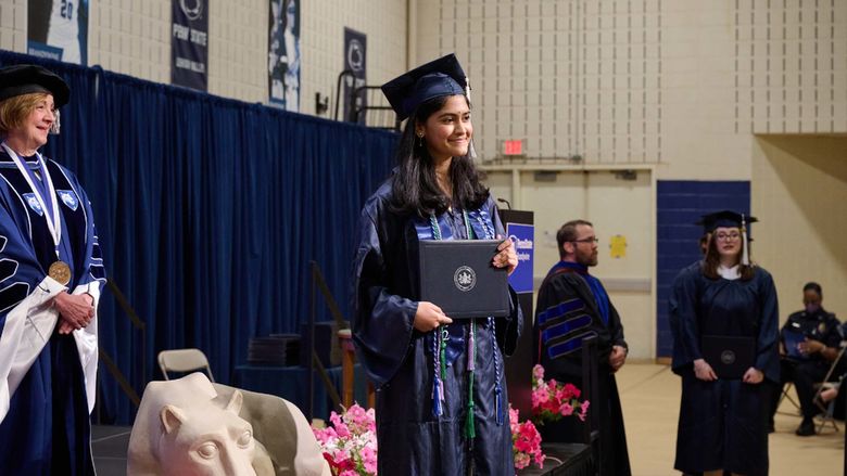 A woman stands on a stage holding a diploma.