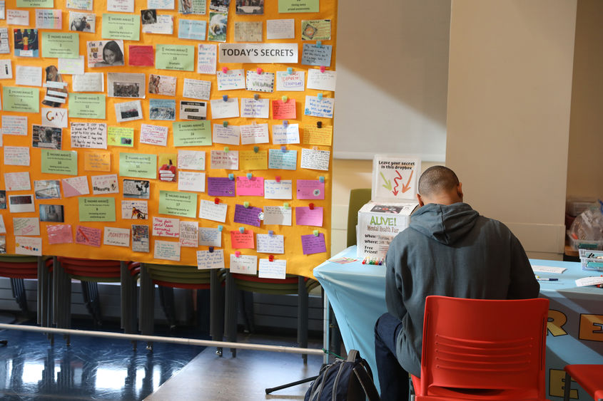 Student writing notecard for "Share a Secret" wall display