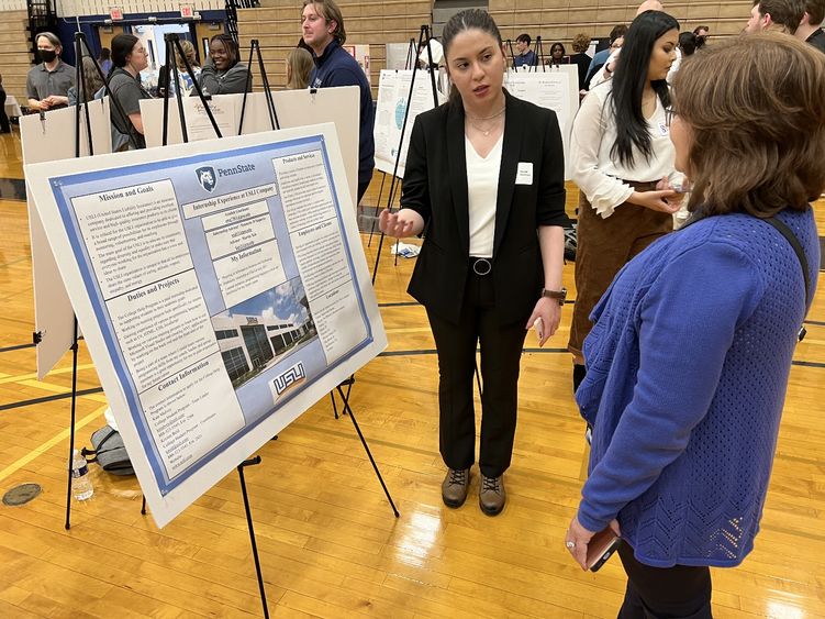 A woman stands next to her internship poster and explains it to another woman.