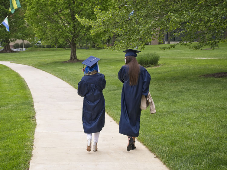 Two students walking while wearing commencement cap and gown.