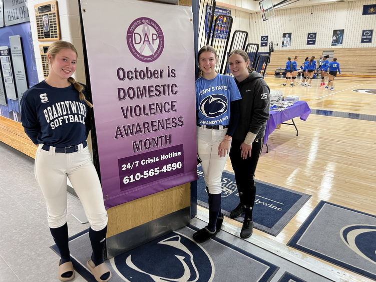 Three female students stand next to a banner that says October is Domestic Violence Awareness Month.