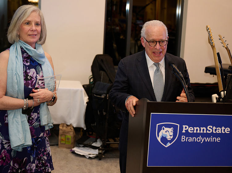 A man speaks at a lectern while a woman stands to his side holding an award.