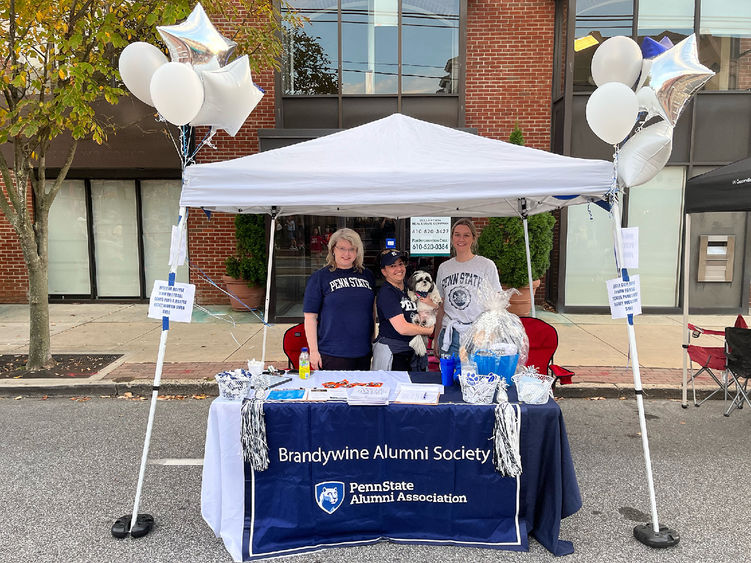 three women standing under a white tent, tablecloth says Brandywine Alumni Society
