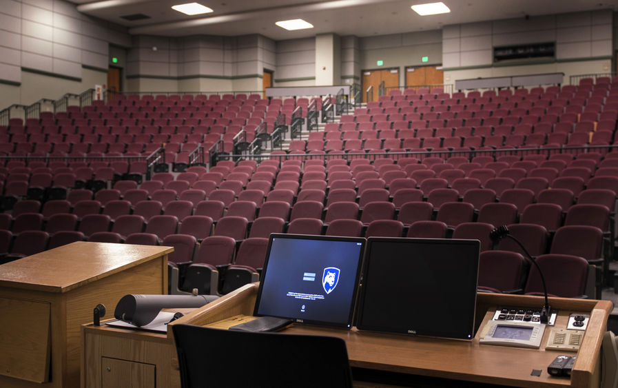 A computer screen is lit up at a podium overlooking an empty theater classroom.