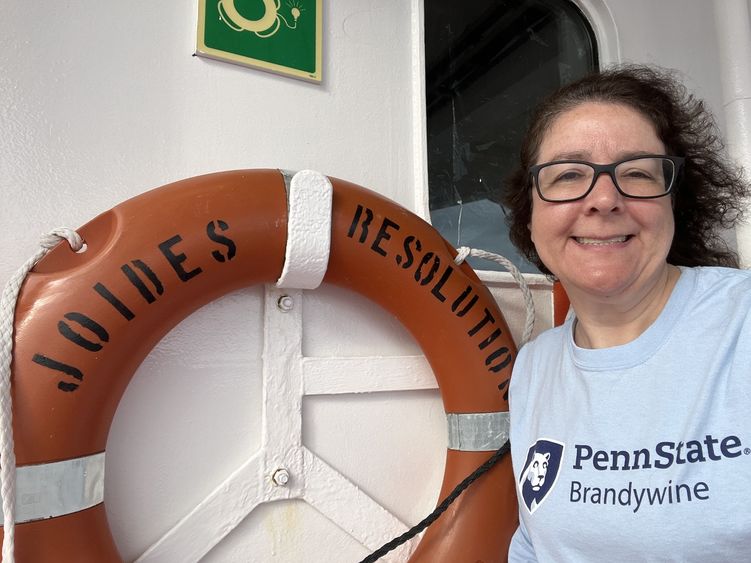 A woman stands next to a life preserver on a ship.