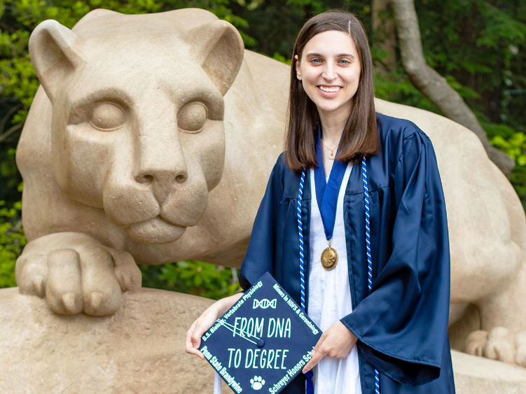 Dana Hallahan in blue cap and gown next to Nittany lion shrine at Penn state university park