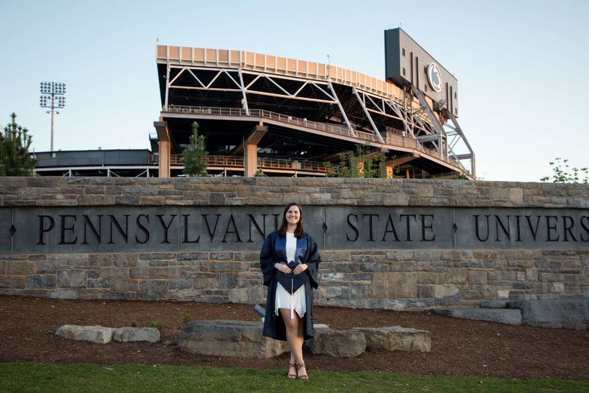 person in cap and gown in front of sports stadium