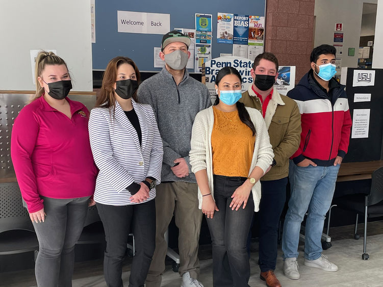 A group of students in masks standing in front of poster boards about their internship experiences. 