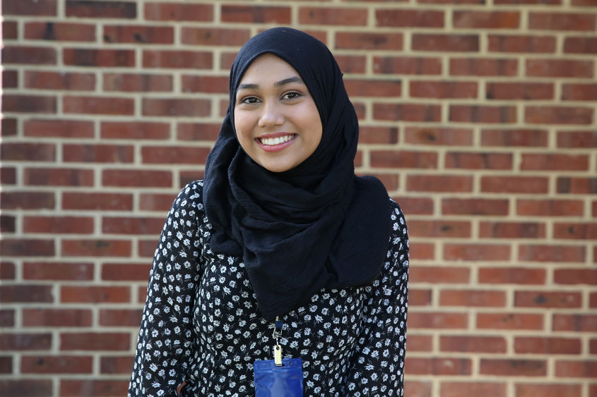 A student standing in front of a brick wall.