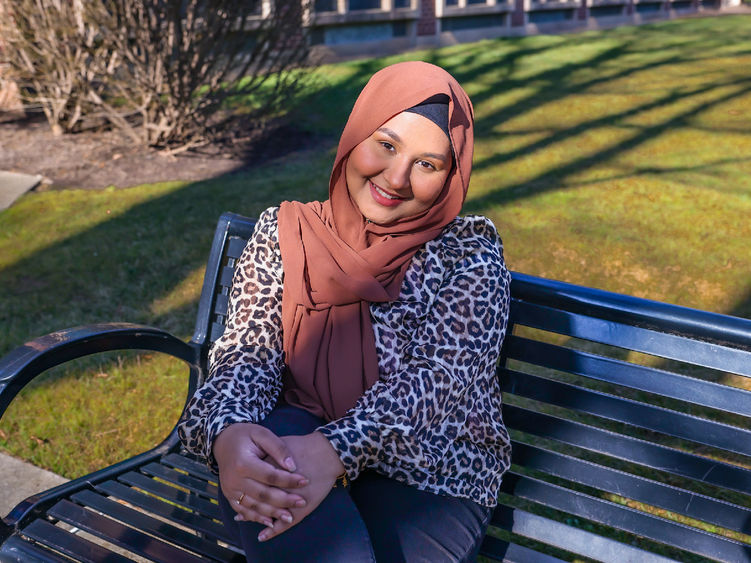 Girl sitting on a bench wearing a cheetah print shirt and pink hijab