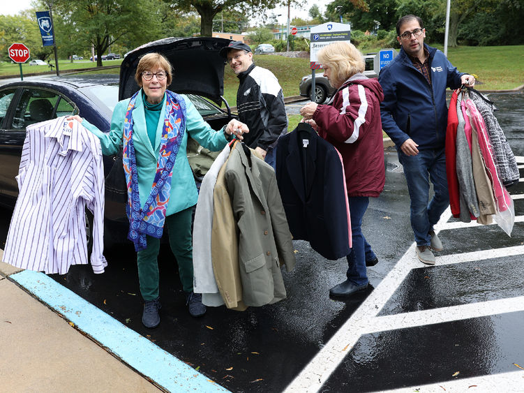 A man takes clothing out of a car trunk and hands it to three other adults.