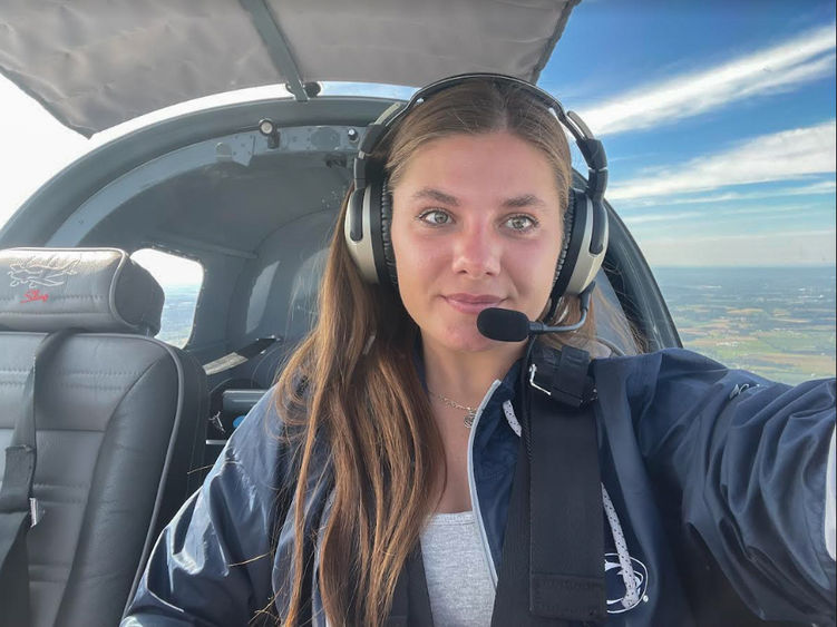 A female sits in the cockpit of a small plane.