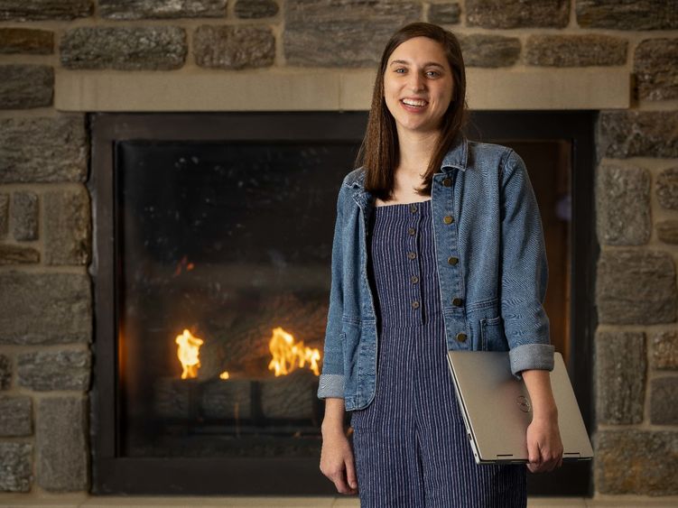 A female stands in front of a fireplace holding a laptop.