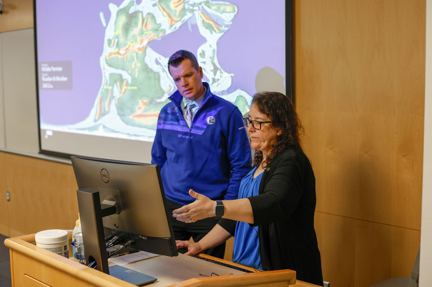 A professor points to a computer to explain an earthquake to a television news reporter.