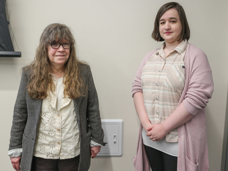 Two women stand in front of a wall in a conference room.