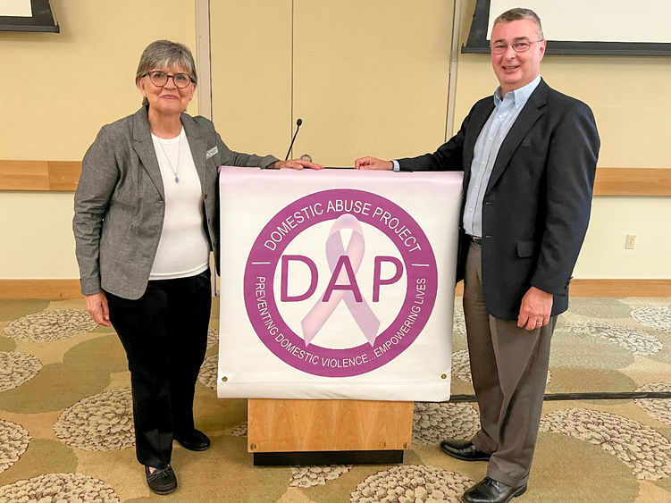 A woman and a man stand next to a lectern with a Domestic Abuse Project banner in the center.