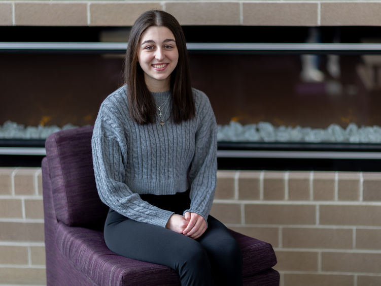 A female student sits on a chair in front of a fireplace.