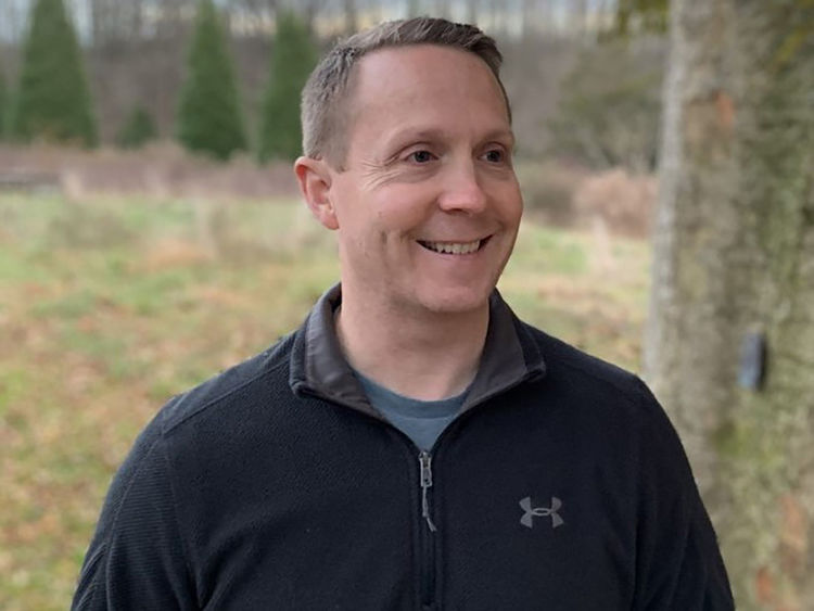 Daniel Hamilton stands outside with trees in the background