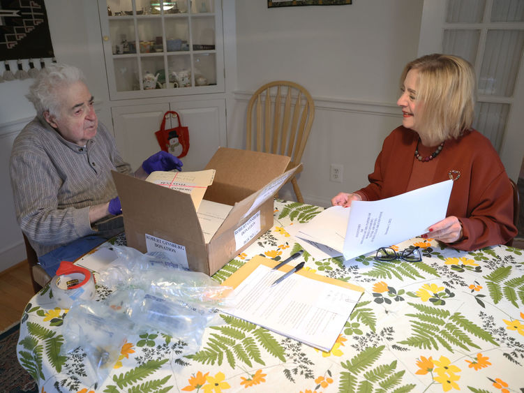 A man and a woman sit at a dining room table look at files.