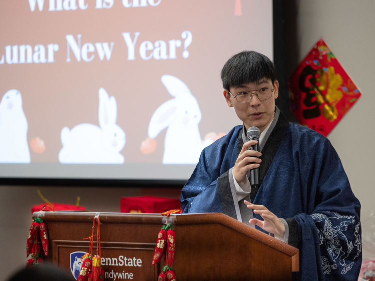A male student stands at a podium wearing a traditional Chinese robe.