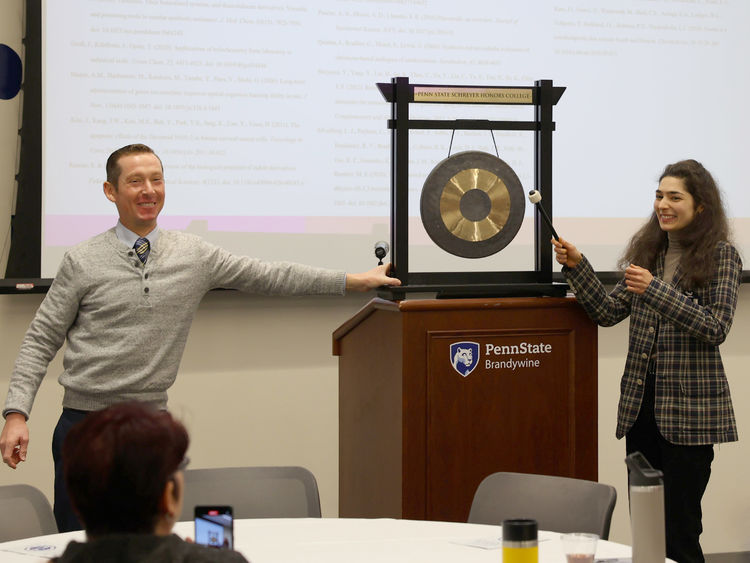 A female student bangs a gong while a male holds it.