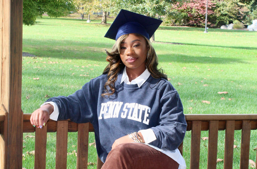 A students wearing a graduation cap sitting on an outside bench.